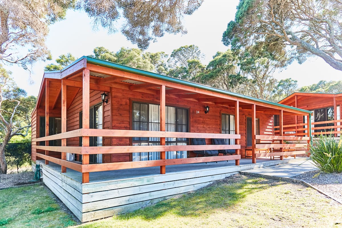 Una cabaña de madera con porche, ventanas amplias y una puerta.