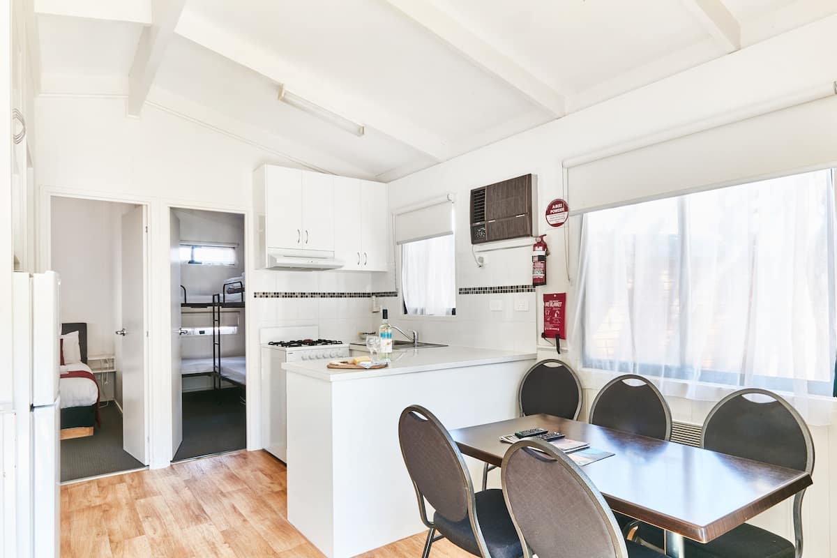 Una cocina compacta con armarios blancos, una isla central y una zona de comedor con cuatro sillas.