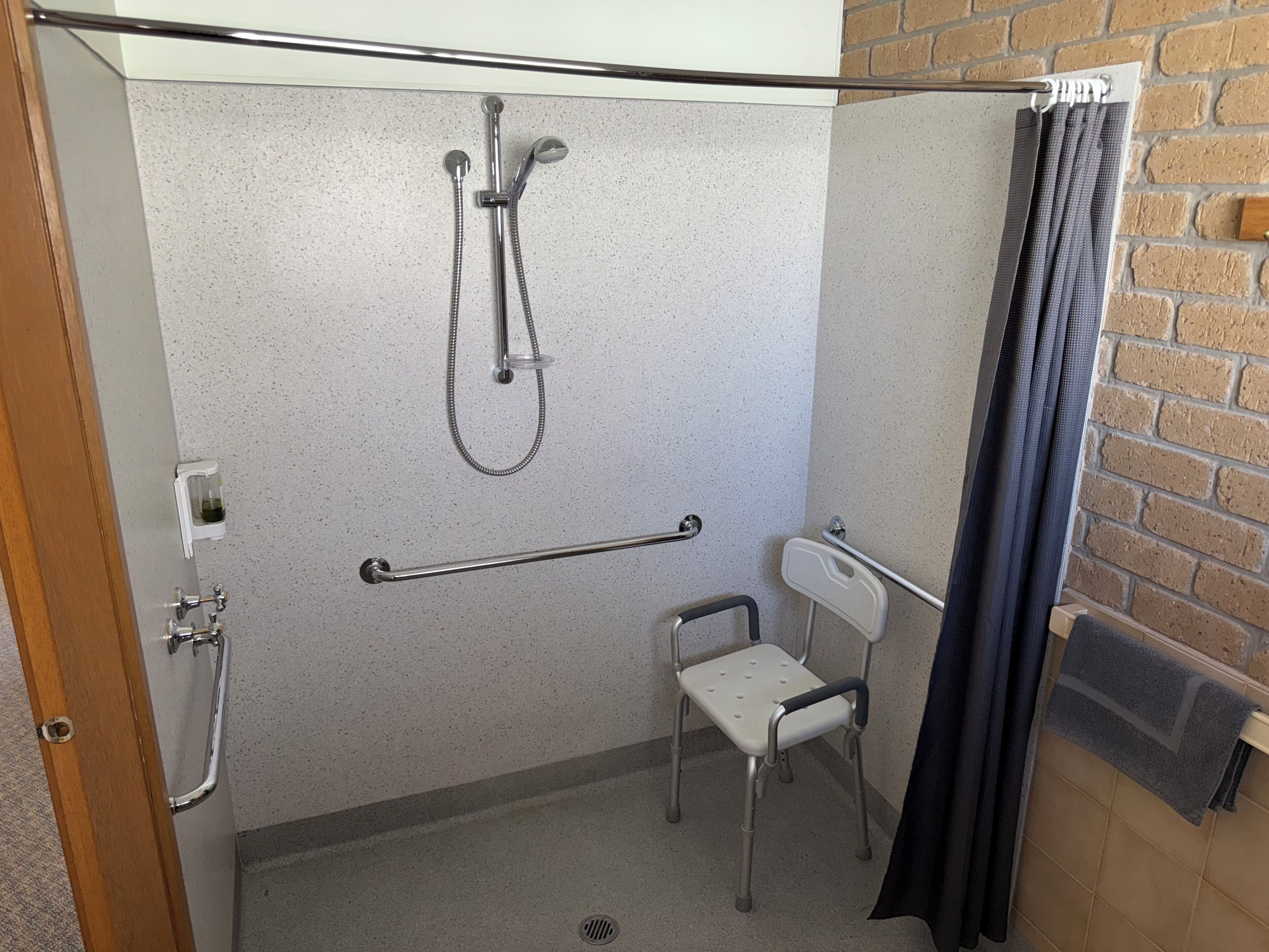 A small, accessible shower room with a grab bar, a wheelchair-accessible chair, and a showerhead.