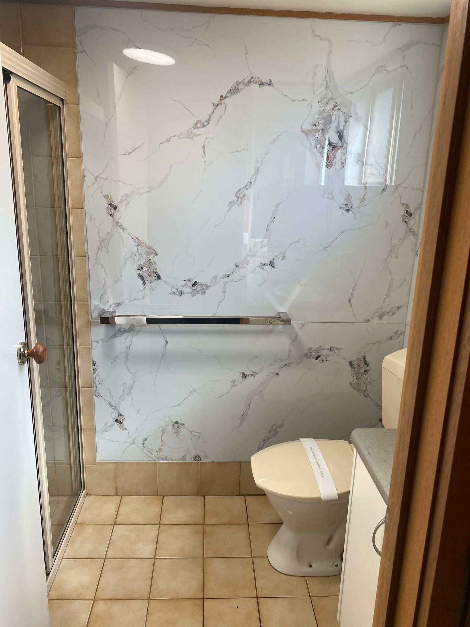 Een badkamer met een marmeren wand, toilet en douche.