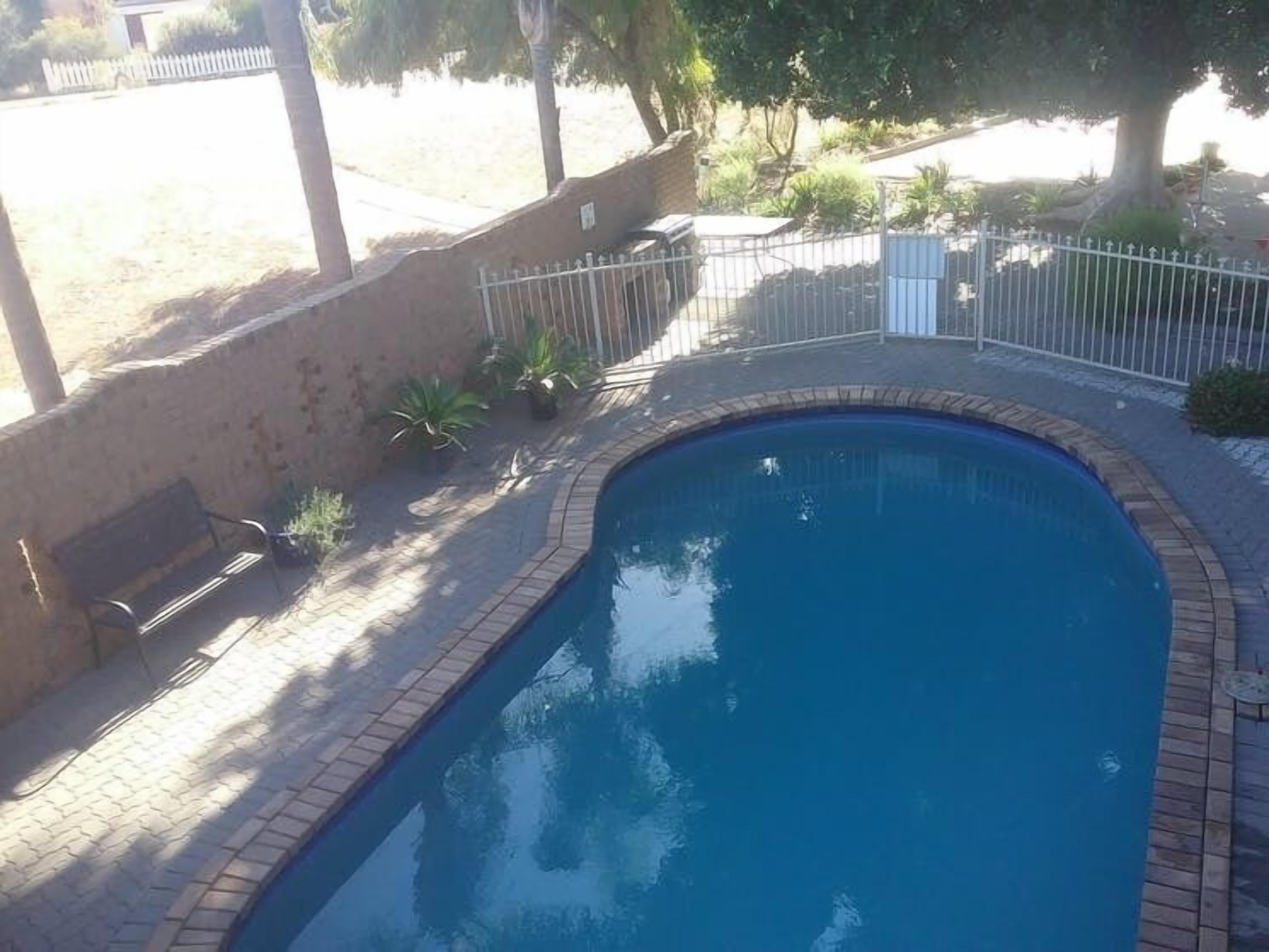 A small, rectangular swimming pool with a brick border, surrounded by a metal fence and a bench.