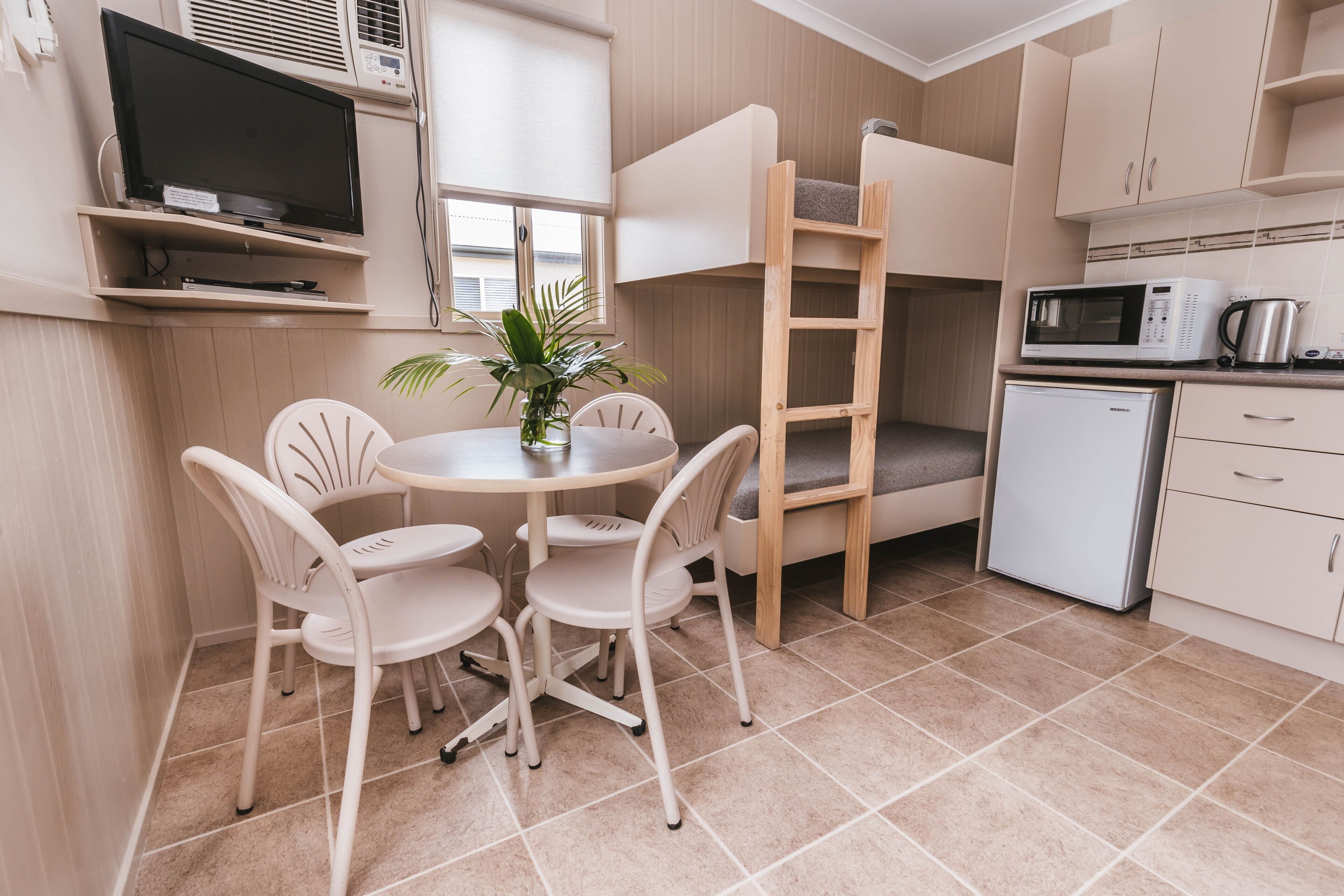 A compact kitchen with a bunk bed, a small refrigerator, a microwave, and a dining area with chairs and a table.