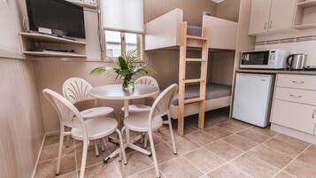 A compact kitchen with a bunk bed, a small refrigerator, a microwave, and a dining area with chairs and a table.