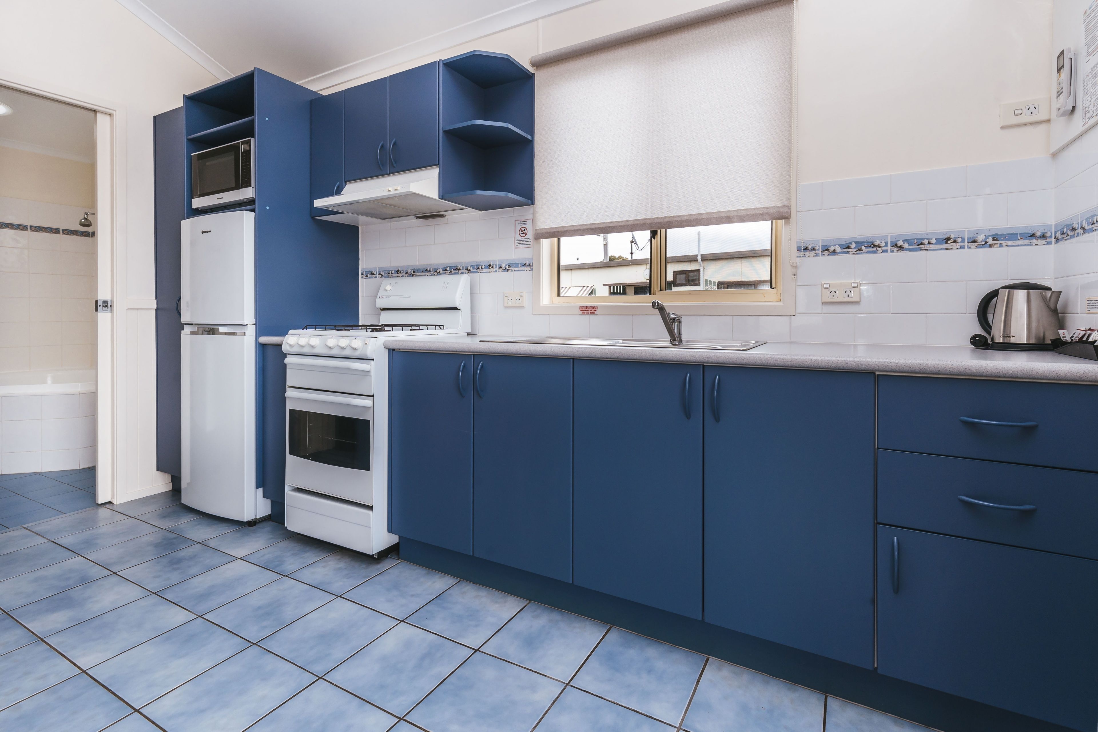 A kitchen with blue cabinets, a white stove, and a window above the sink.