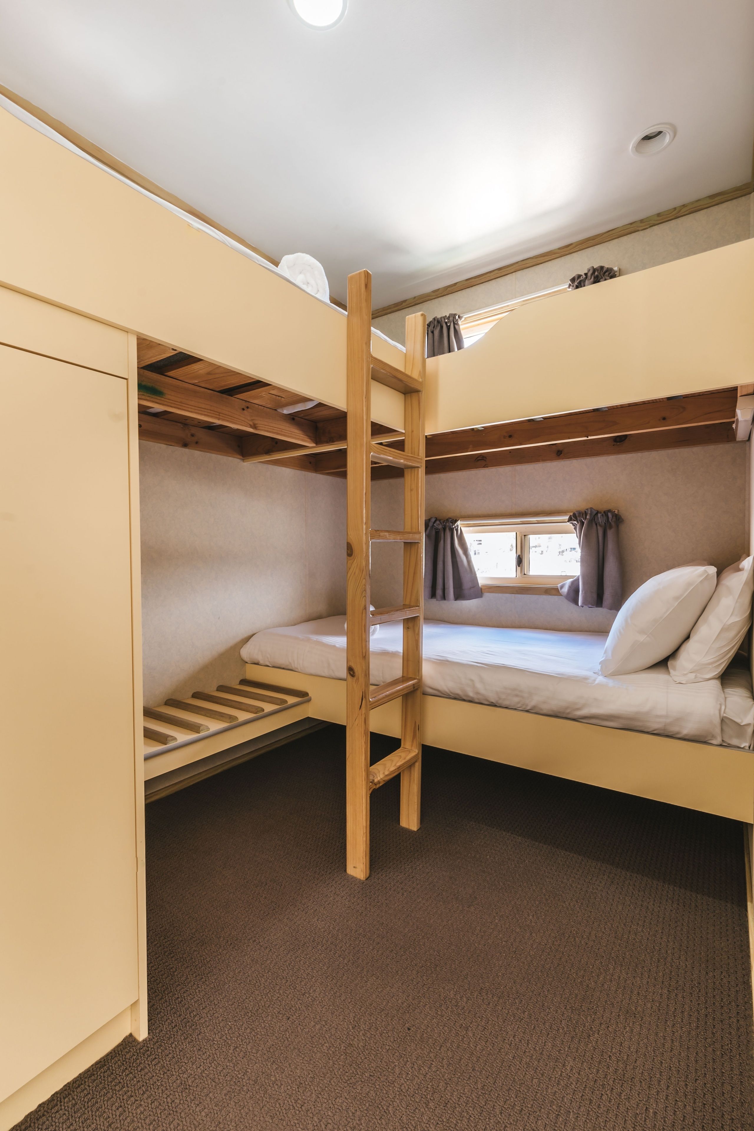 Uma cama beliche com escada, uma janela com cortinas e um guarda-roupa.
