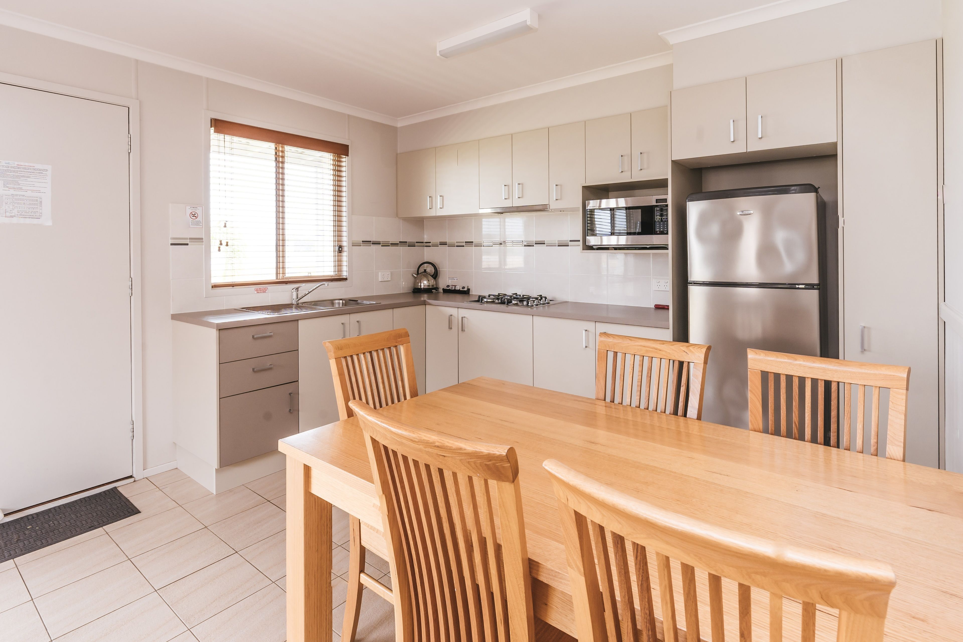 A modern kitchen with a wooden dining table and chairs, stainless steel appliances, and light-colored cabinetry.