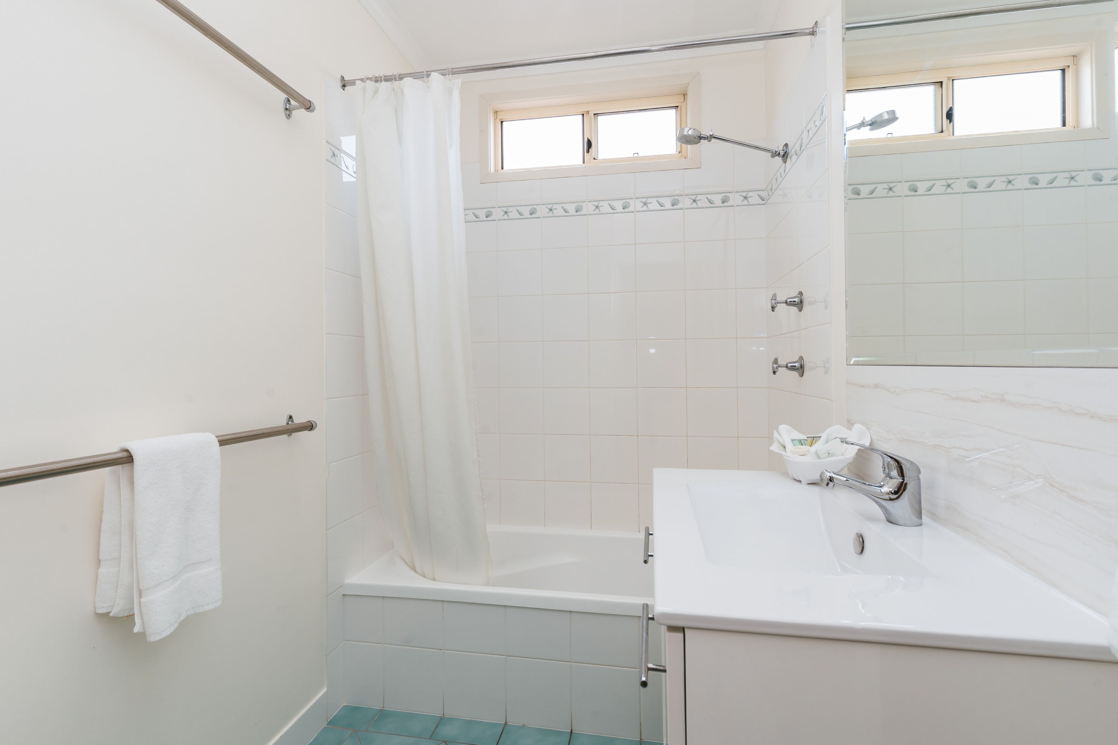 Un baño con bañera, cortina de ducha, ventana, lavabo y toallero.