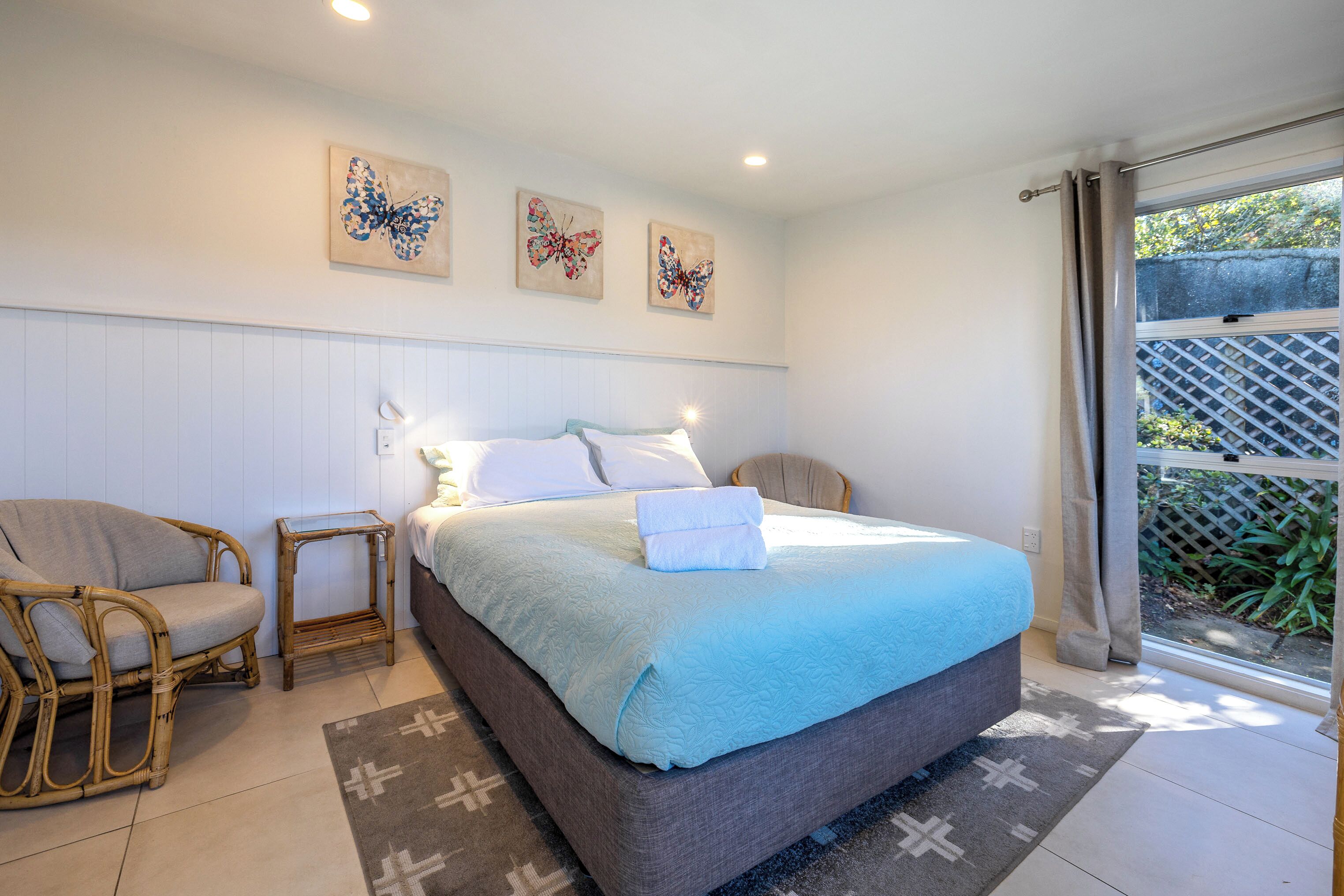 A bedroom with a bed, two chairs, a nightstand, and three butterfly wall art pieces.
