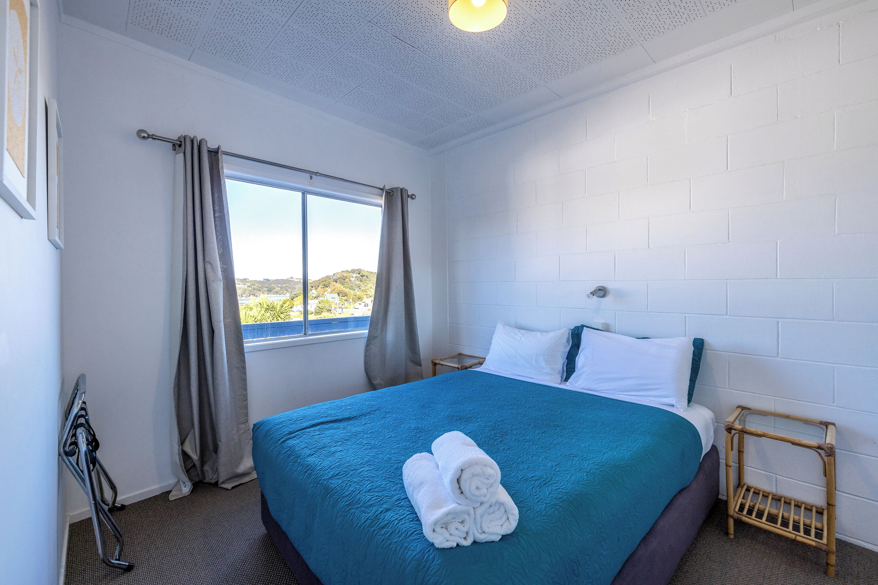 Habitación de hotel con una cama grande, una ventana con cortinas, una mesita de noche pequeña y vistas al exterior.