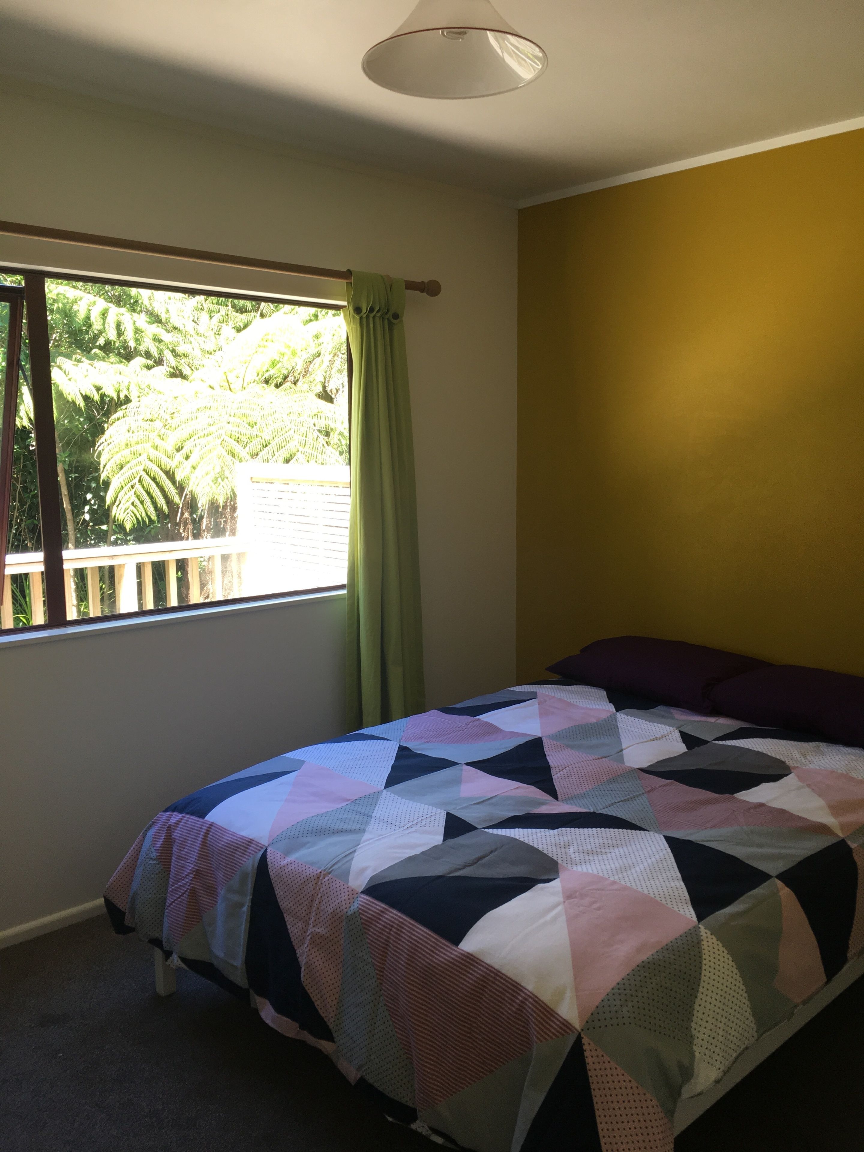 Une chambre à coucher avec un lit, une fenêtre avec des rideaux, une vue sur la verdure et un mur jaune.