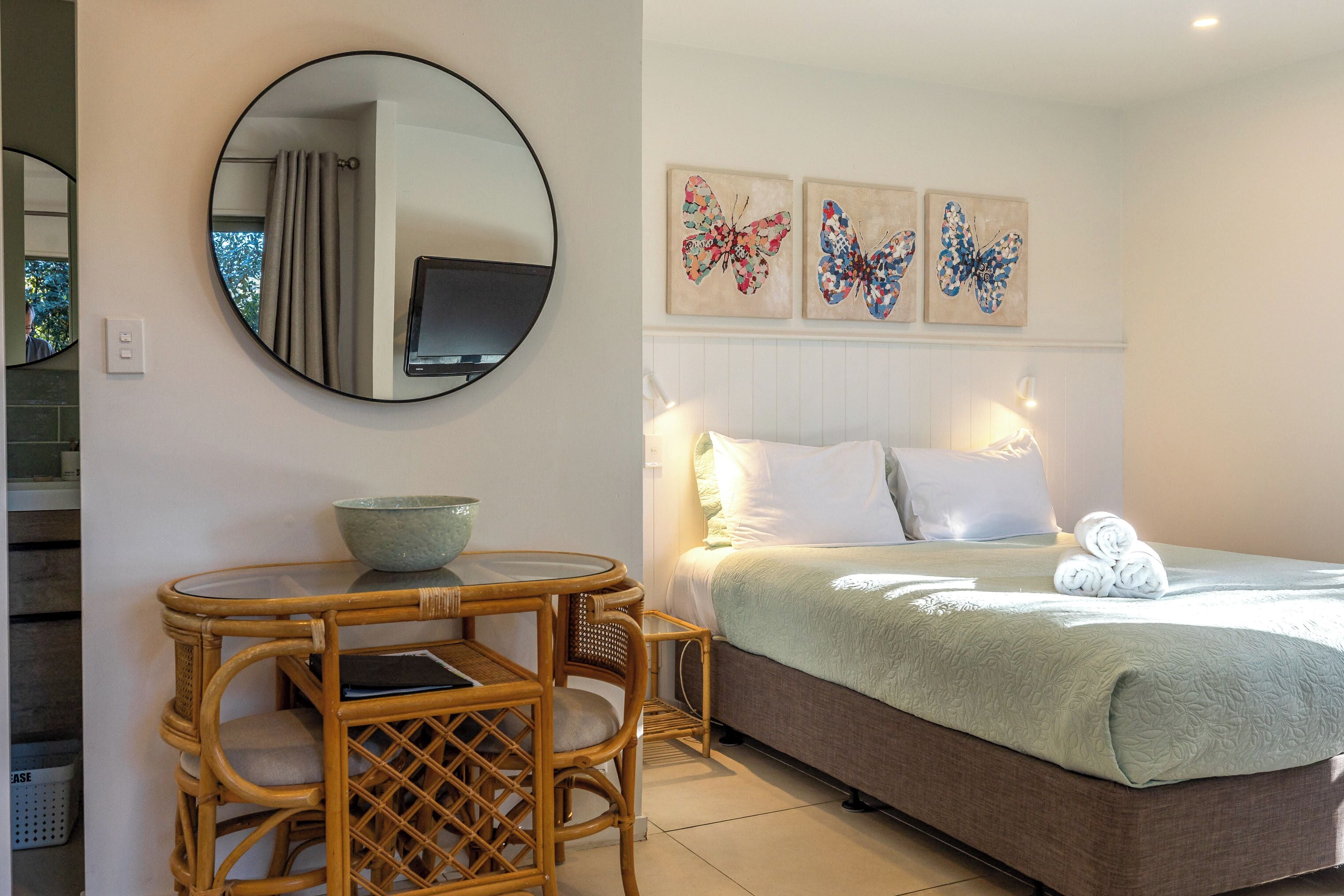 A bedroom with a bed, a round mirror, a small table with chairs, and artwork on the wall.