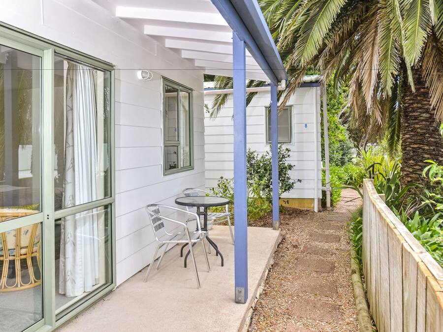 A covered patio with a table and chairs, a wicker chair, and a glass door leading to a room.