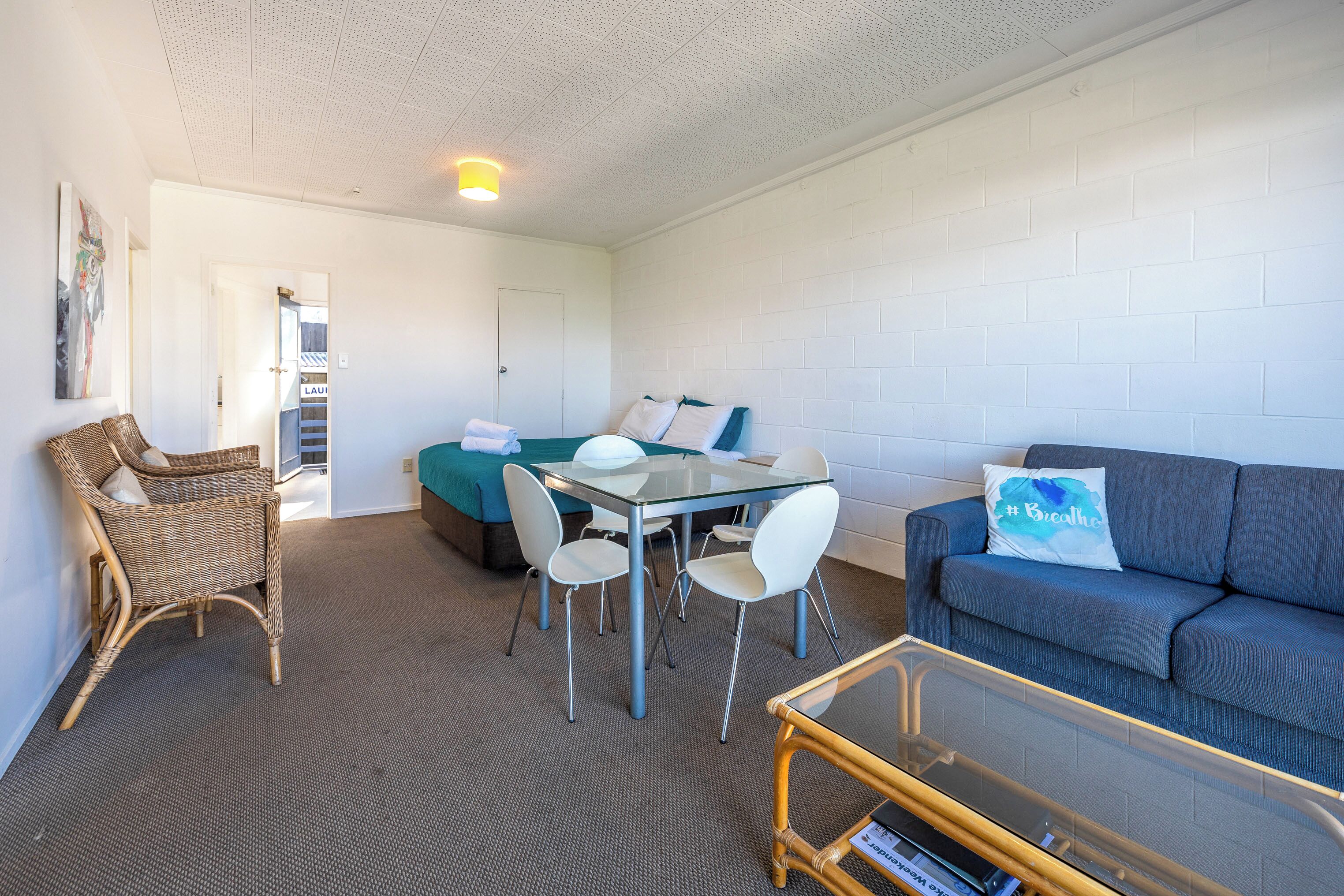 A compact room with a glass-top table, white chairs, a blue sofa, and a wicker chair.