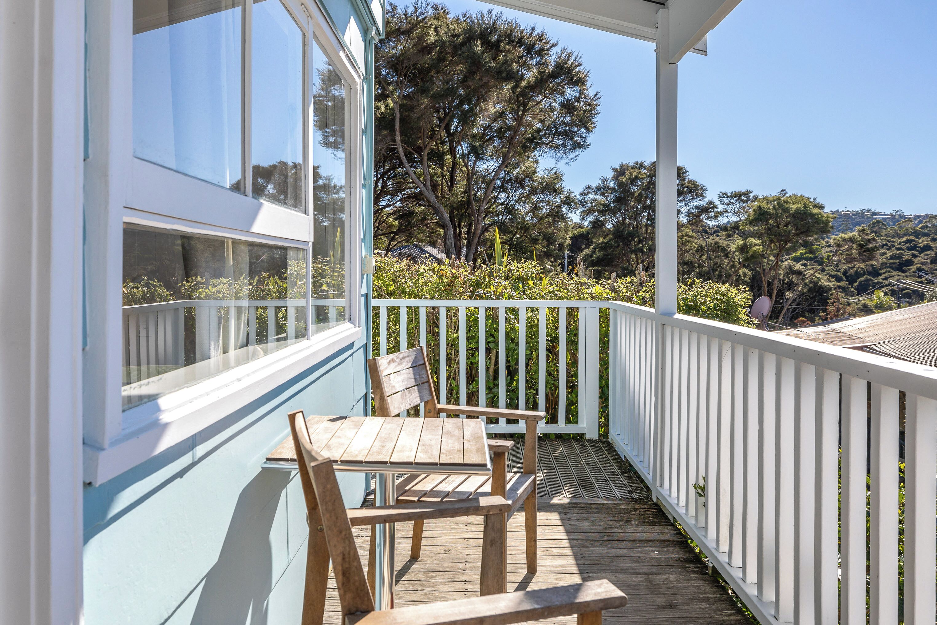 A wooden deck with a table and chairs, white railings, and a view of trees and hills.