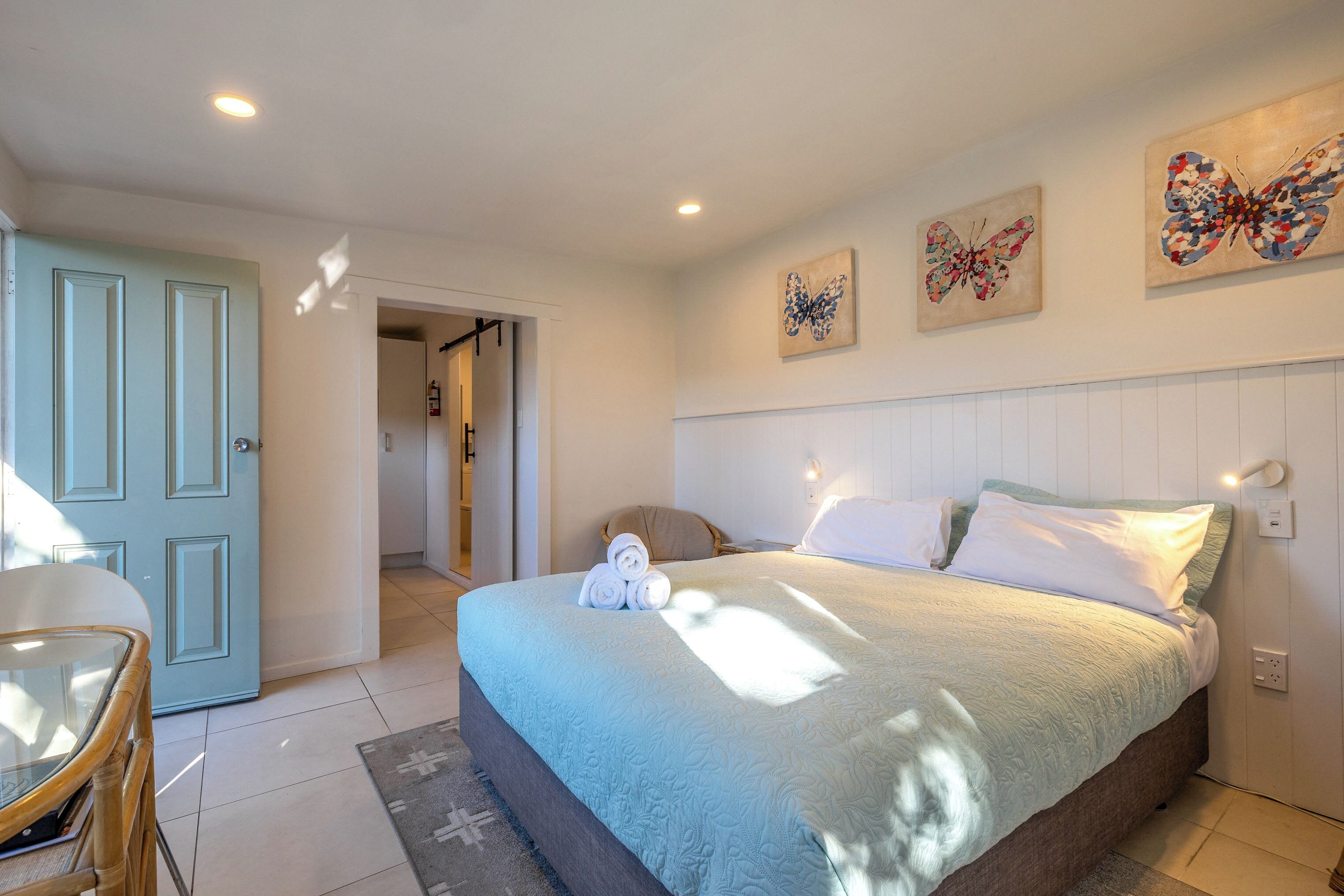 Un dormitorio con cama, almohadas, mesita de noche y una obra de arte en la pared.