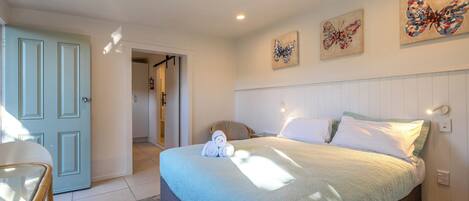 Un dormitorio con cama, almohadas, mesita de noche y una obra de arte en la pared.