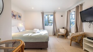 A hotel room with a bed, a television, a chair, and a window with curtains. - Waiheke Island Motel (Waiheke Island)