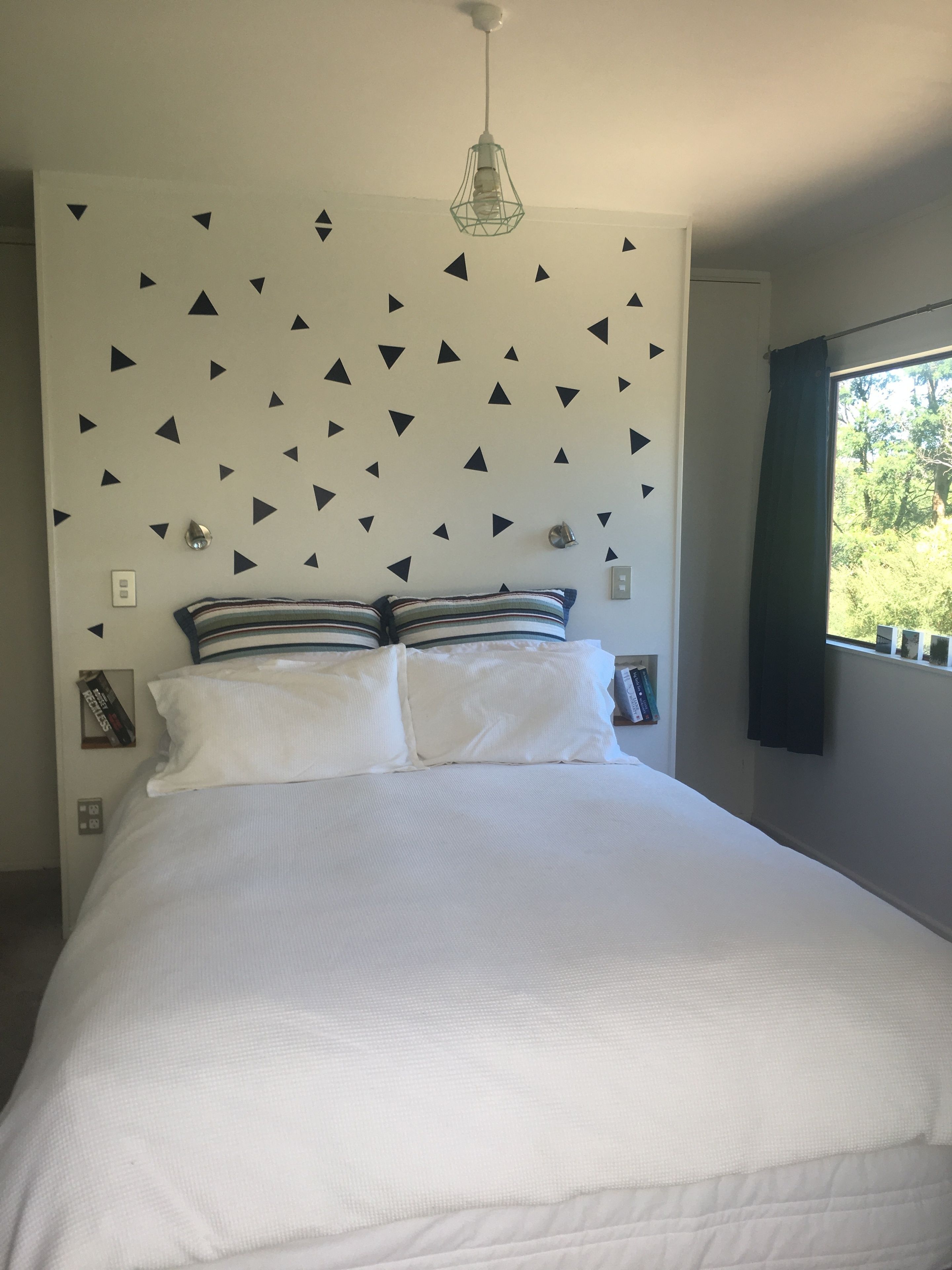 A bedroom with a bed, pillows, a wall-mounted light fixture, and a window with curtains.
