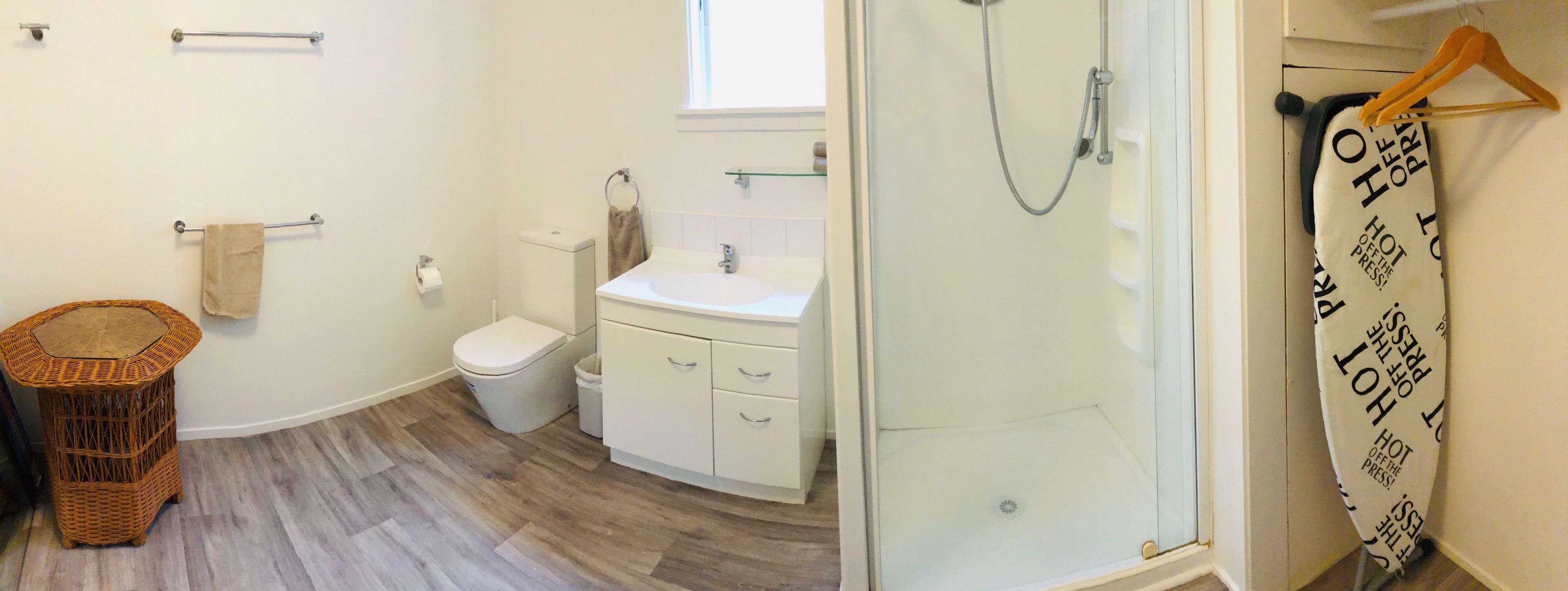A bathroom with a white sink, toilet, and shower. There is a wicker basket and a towel rack on the wall.