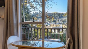 A balcony with a glass table and white chair, overlooking a scenic view of a town and hills. - Waiheke Island Motel (Waiheke Island)