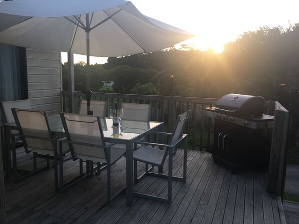 Una terraza con mesa, sillas, una parrilla y una sombrilla.