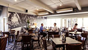A restaurant with wooden tables and chairs, a patterned carpet, and a large wall mural.