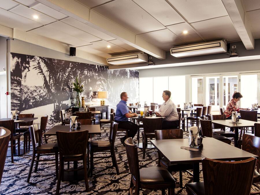 A restaurant with wooden tables and chairs, a patterned carpet, and a large wall mural.
