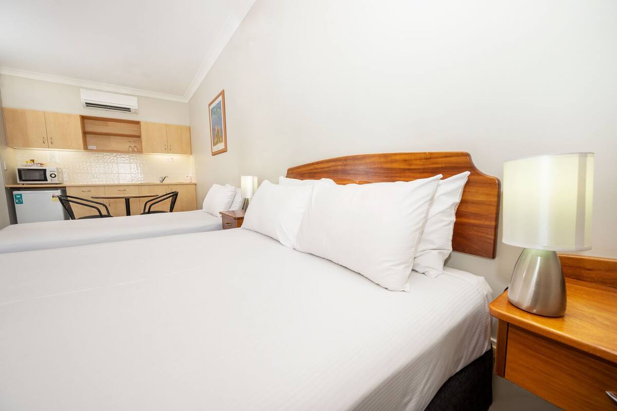 A hotel room with a bed, a bedside table with a lamp, a small kitchenette with a microwave, and a refrigerator.