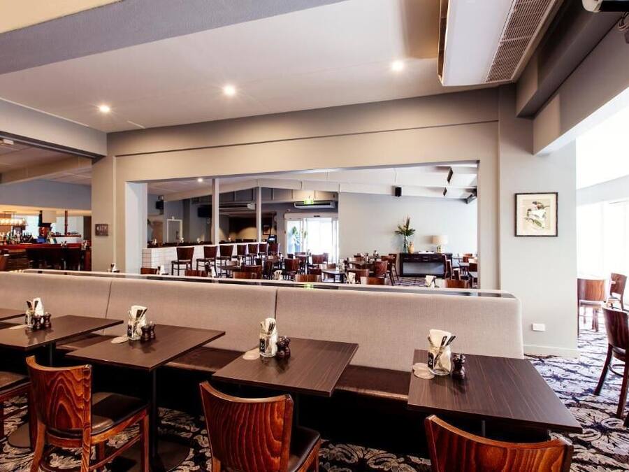 Un restaurante con varias mesas y cabinas, un espejo grande que refleja el interior, y una zona de cocina visible.