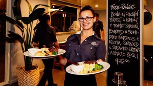 A person holding a plate with food and a chalkboard menu listing specials. - Shamrock Gardens Motel (West Mackay)