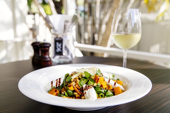 A white plate of food on a dark wooden table with a glass of white wine and a salt and pepper shaker in the background. - Shamrock Gardens Motel (West Mackay)