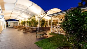 An outdoor patio area with a covered seating area, tables, and chairs, surrounded by greenery and plants. - Shamrock Gardens Motel (West Mackay)