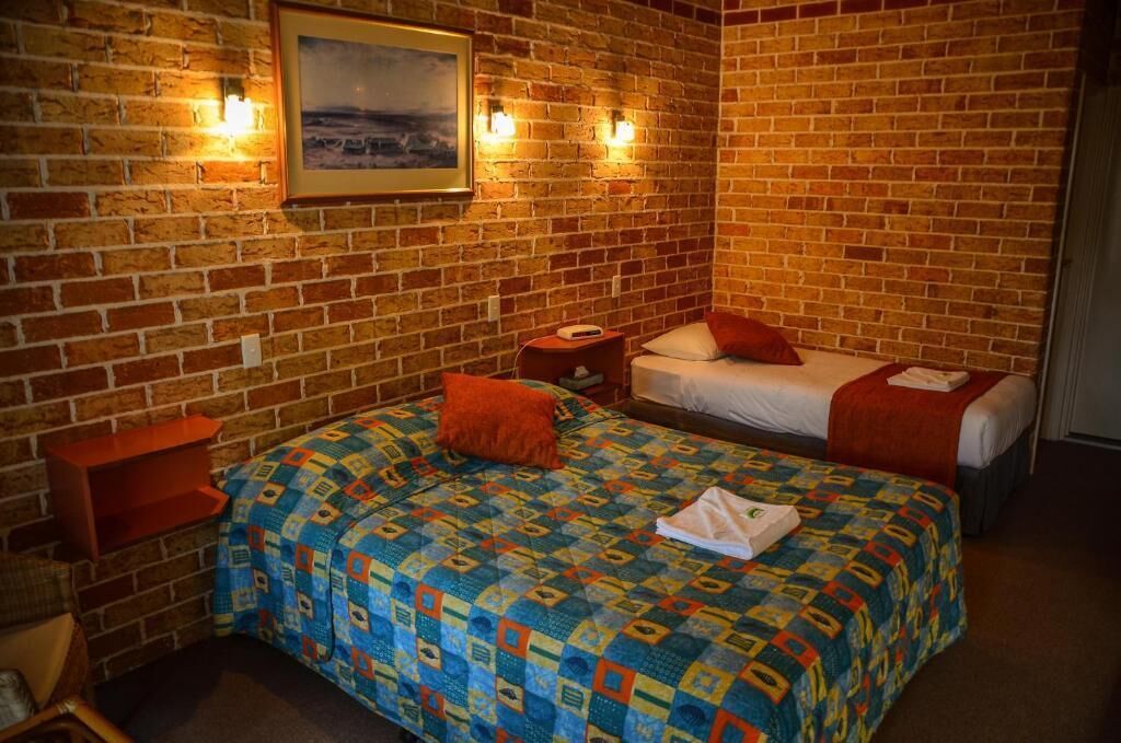 A room with a brick wall, two beds with colorful bedding, a small table, and a framed picture on the wall.