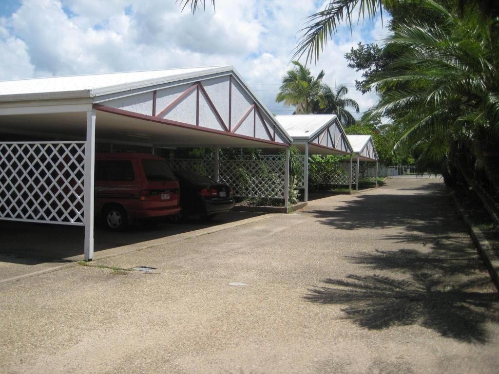 A covered parking area with a red vehicle parked under a white lattice structure.
