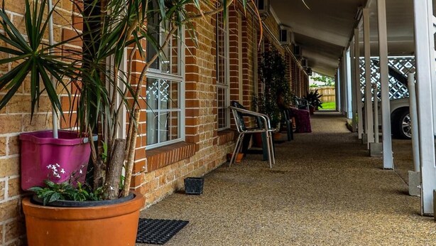A covered corridor with brick walls, potted plants, and air conditioning units. - Beenleigh Village Motel (Beenleigh)