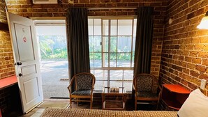 A hotel room with a patterned carpet, a bed with rolled towels, two chairs, a table, a door, and a window with curtains. - Beenleigh Village Motel (Beenleigh)