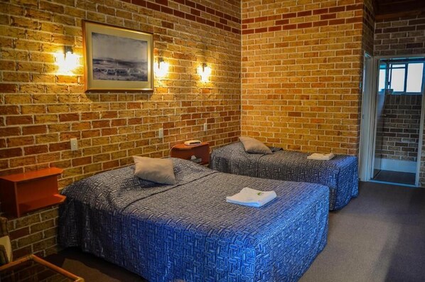 A room with two beds, a brick wall, a framed picture, and a nightstand. - Beenleigh Village Motel (Beenleigh)