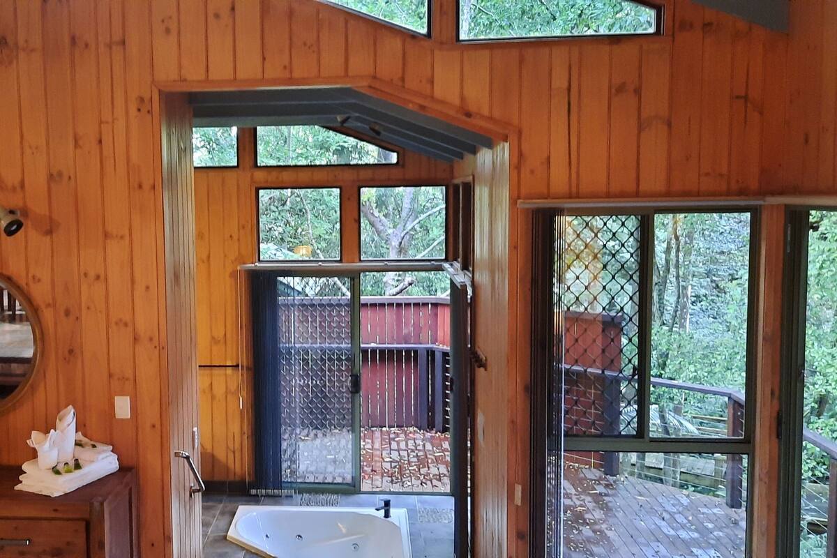 A wooden cabin with a bathroom featuring a sink, mirror, and a large window.