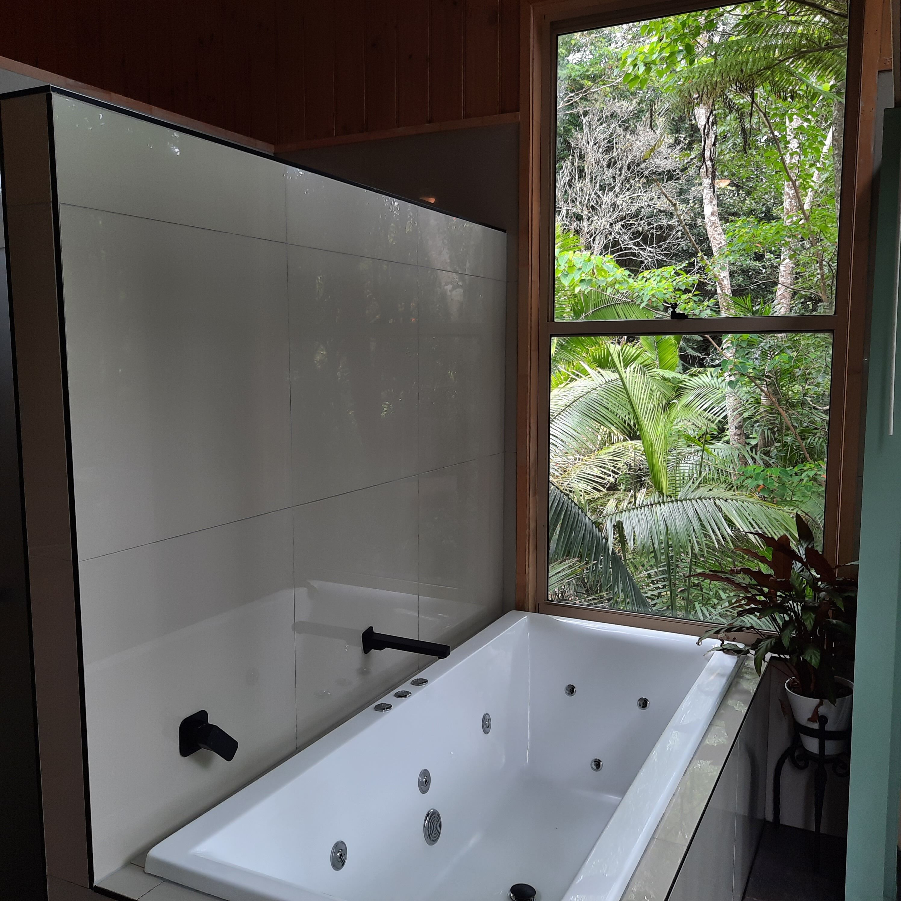 Un baño con bañera, ventana con vistas a la vegetación y una planta en maceta.