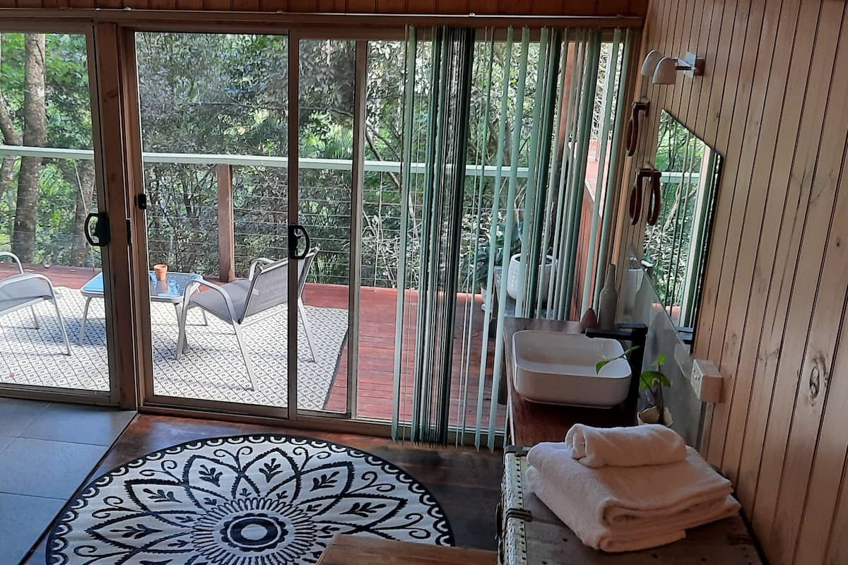 A room with a sliding glass door leading to an outdoor deck with a table and chairs, a small sink, and a decorative rug.