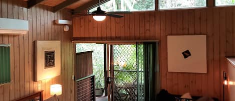 A wooden cabin room with a bed, a couch, and a view of greenery outside.