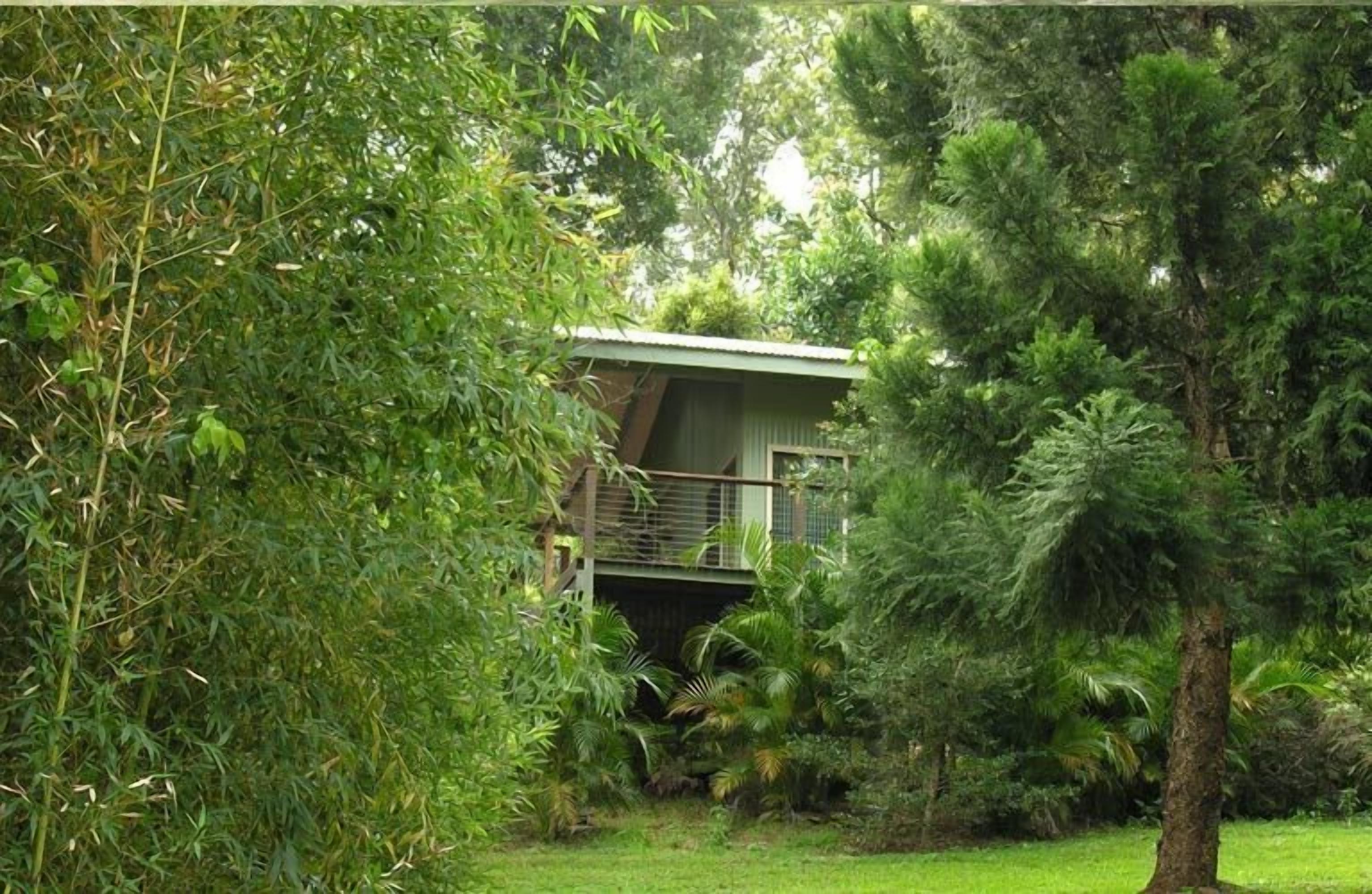 Un petit bâtiment d’un seul étage, entouré d’une végétation luxuriante, avec un balcon visible et une rambarde en métal.