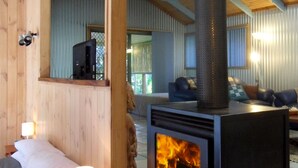 A cozy room with a wood-burning stove, a bed with pillows, a small table with a lamp, and a blue sofa. - Treetops Accommodation Montville (Flaxton)