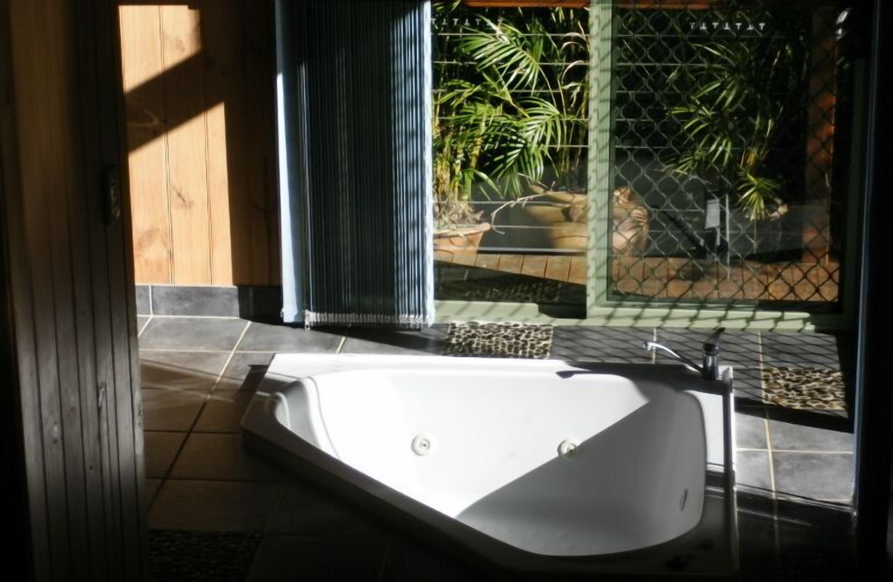 Une salle de bain dotée d’une grande baignoire, d’une douche et d’une fenêtre donnant sur un jardin.