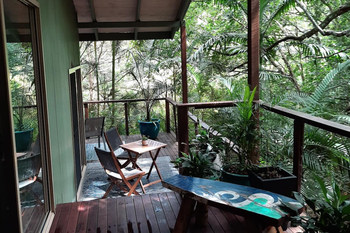 A wooden deck with a table and chairs, surrounded by lush greenery and trees.