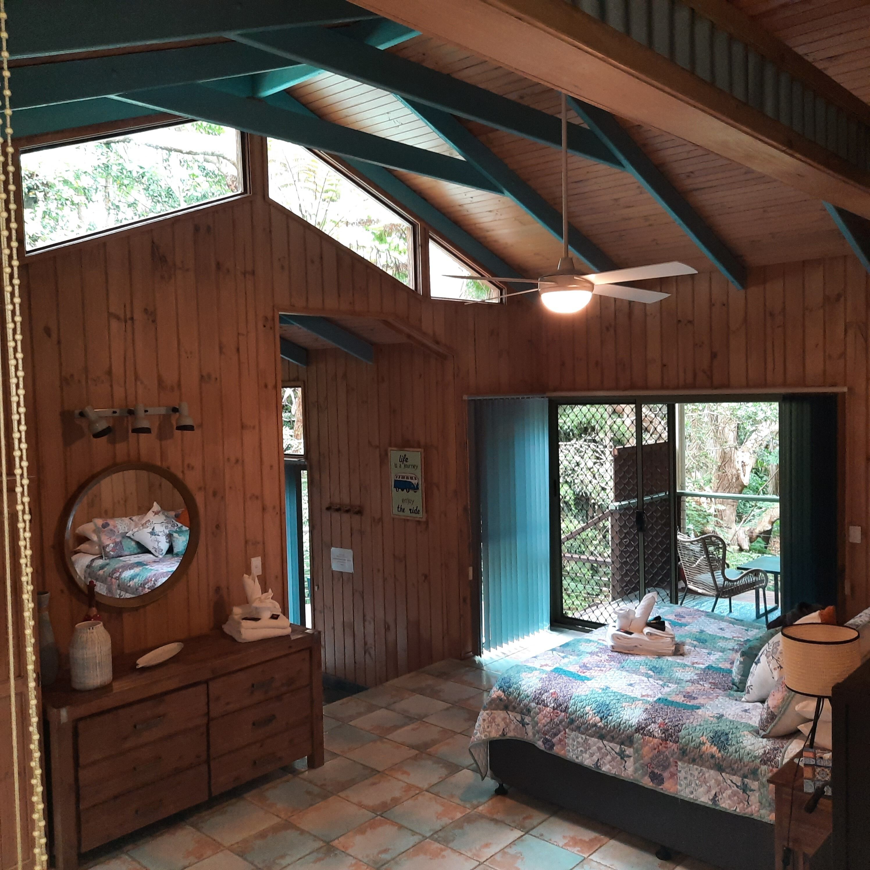 A wooden room with a bed, a dresser, a mirror, and a ceiling fan.