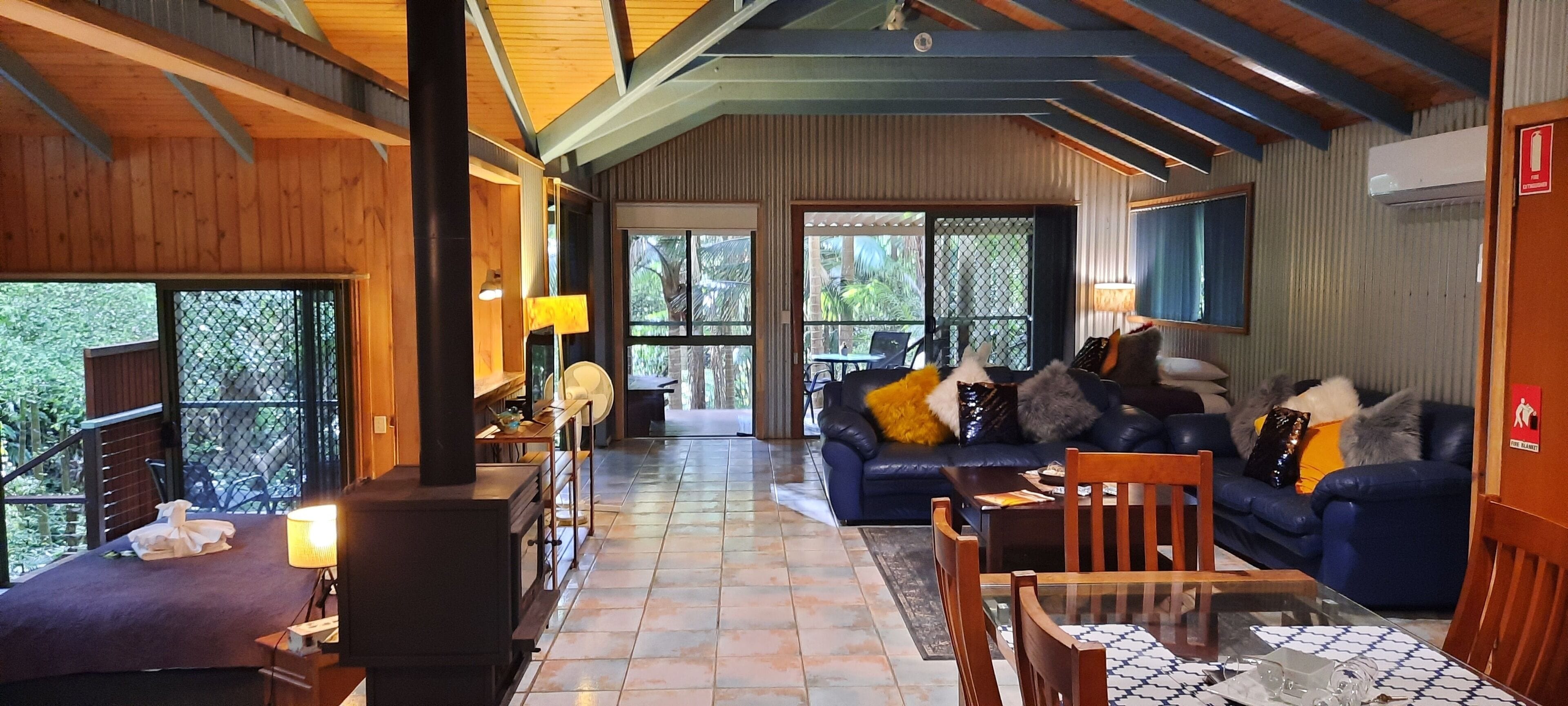 A spacious living area with a fireplace, a sofa with decorative pillows, a dining table with chairs, and large windows offering a view of the outdoors.