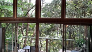 A room with large windows offering a view of a lush garden. There is a seating area with a table and chairs. - Treetops Accommodation Montville (Flaxton)