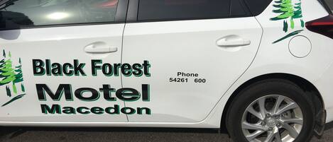 Une voiture blanche avec l’inscription « Black Forest Motel Macedonia » et un numéro de téléphone sur le côté.