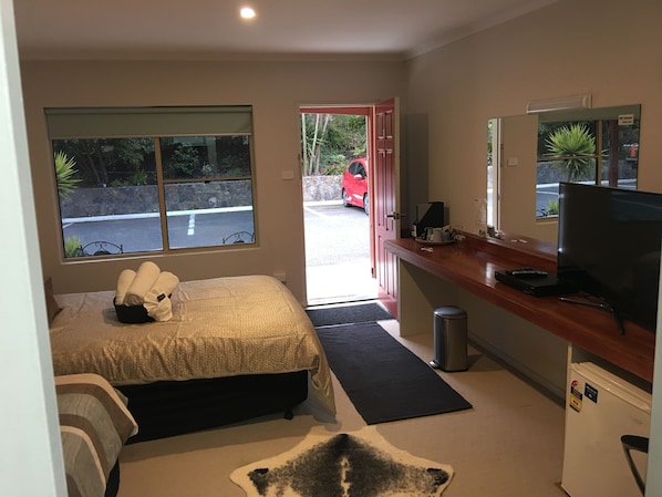 Un dormitorio con cama, mesita de noche, televisor y un refrigerador pequeño.